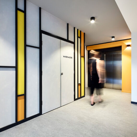 Bayswater Women's Housing blurred figure walking towards lift through foyer space with yellow abstract wall designs - building photographer example / concept
