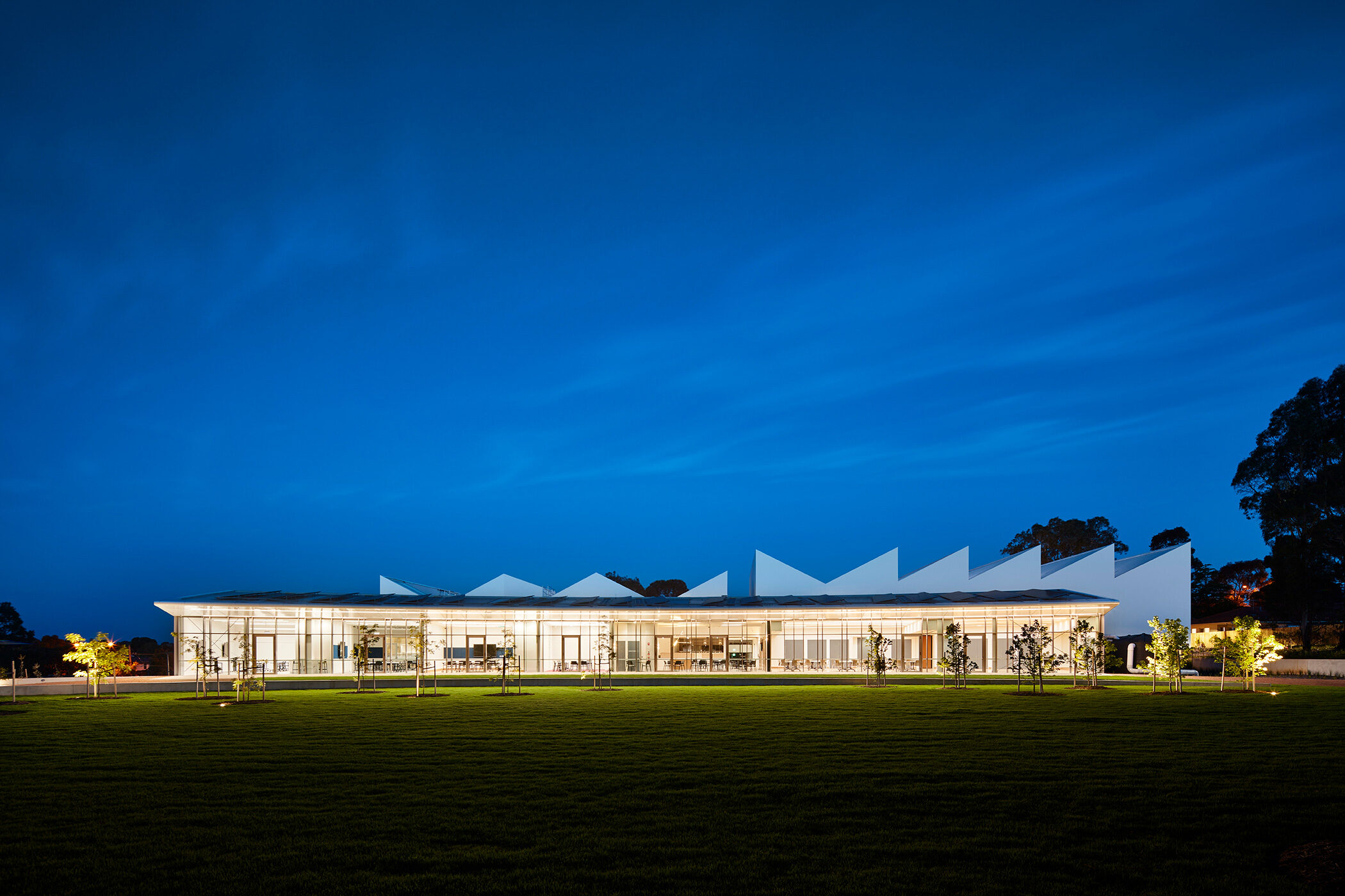 Nunawading Community Hub glazed facade at night with asymmetric sawtooth roofline rising up behind - structure photographer example / concept